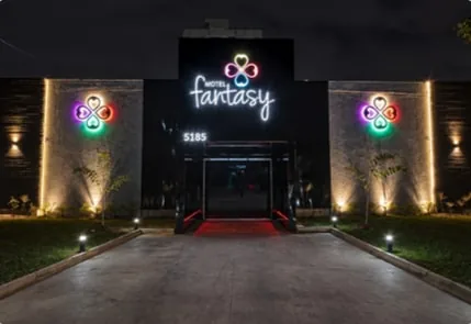 Fachada de uma unidade da Rede Fantasy à noite, com o letreiro em neon e a entrada iluminada