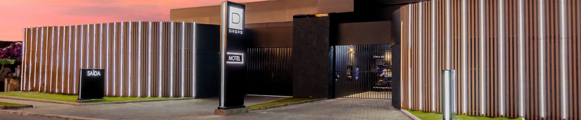 Fachada iluminada de uma unidade da Rede Drops ao entardecer